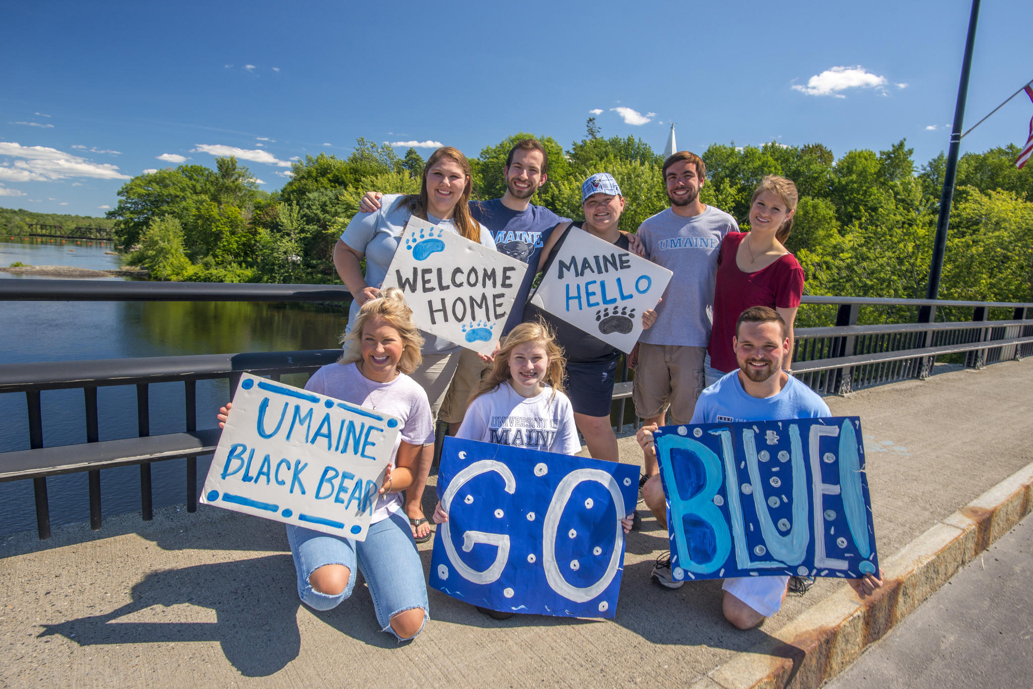 A group of students holding signs welcoming students to campus, two signs in the foreground read Go Blue